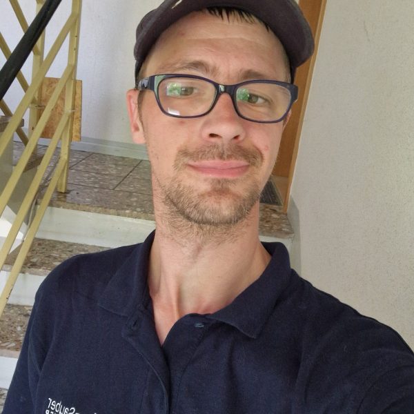 Mann mit Brille und Mütze macht ein Selfie im Treppenhaus, Handwerker Arbeitskleidung.